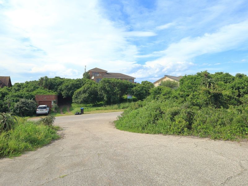 A view of the paved street and access road leading towards the residential property, surrounded by established coastal vegetation.