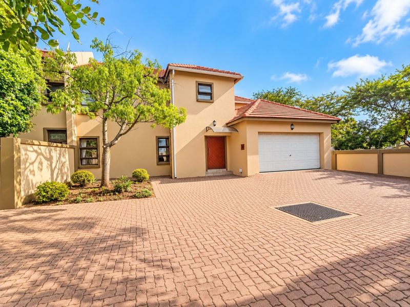 Front elevation of a townhouse featuring a paved driveway, single garage, and well-maintained stucco facade with tiled roofing.