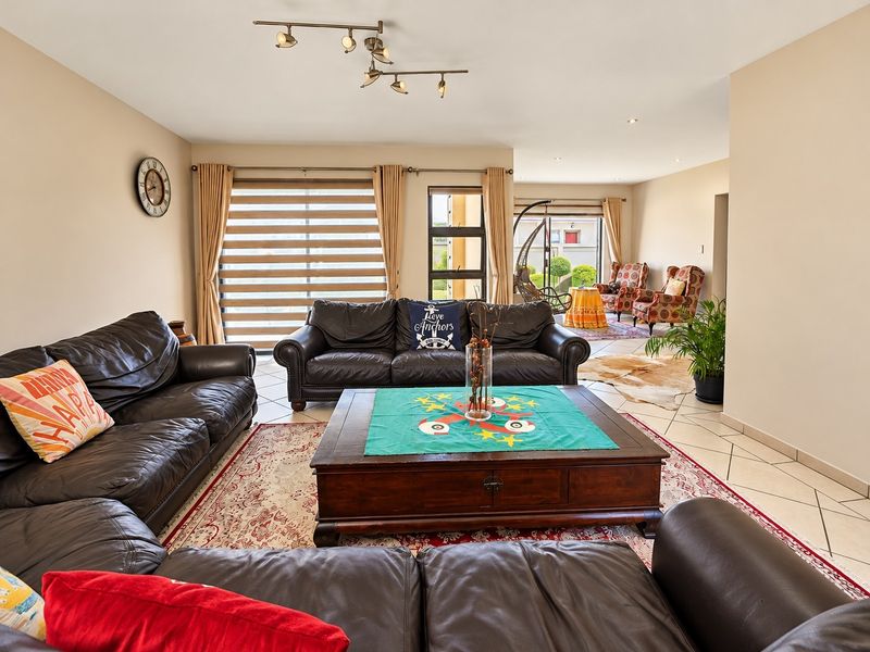 Spacious open-plan living area featuring tiled flooring, modern track lighting, and large windows with blinds, providing ample natural light.