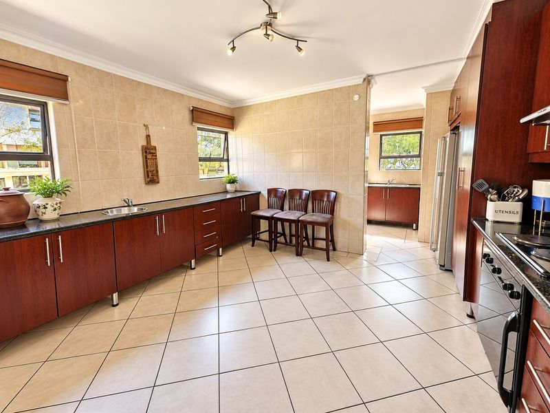 Spacious kitchen featuring dark wood cabinetry, granite countertops, tiled walls and floors, and a separate scullery area for additional prep and storage.