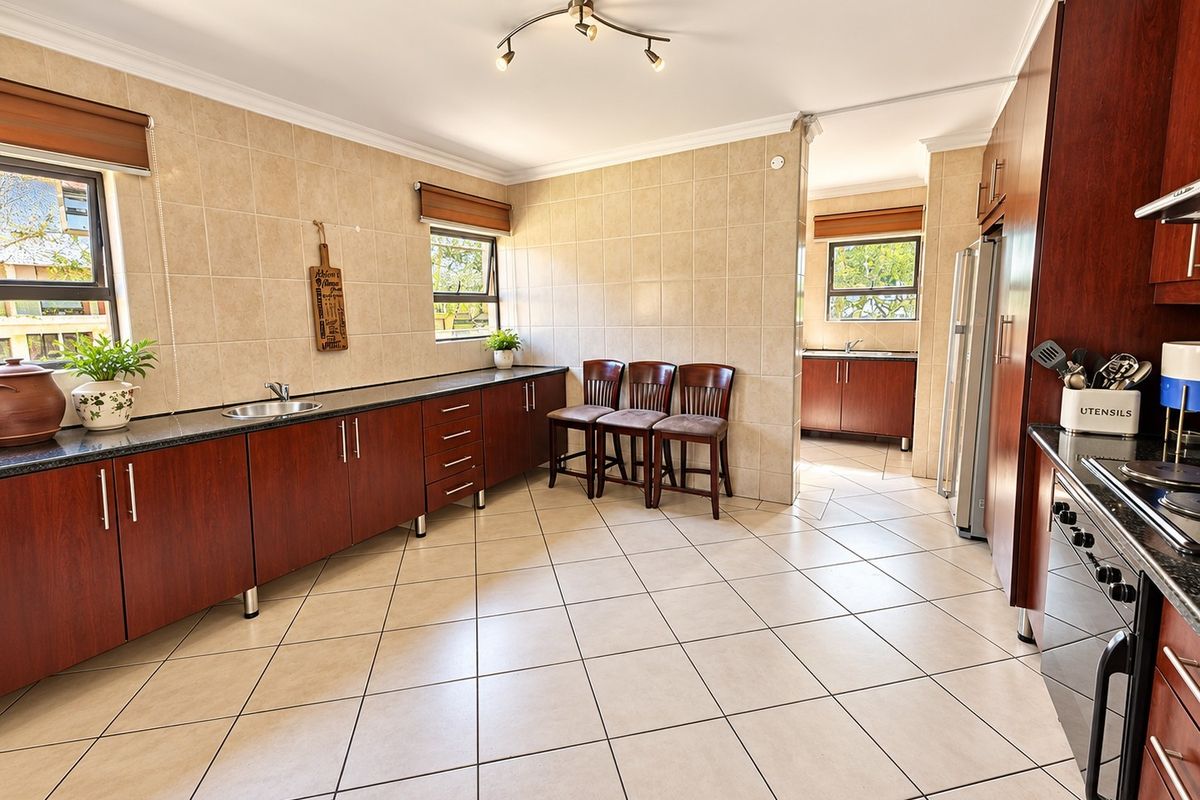 Spacious kitchen featuring dark wood cabinetry, granite countertops, tiled walls and floors, and a separate scullery area for additional prep and storage.