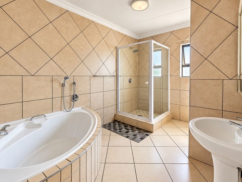 A spacious bathroom featuring a built-in bathtub, a separate shower enclosure, and a pedestal basin with neutral wall and floor tiling.