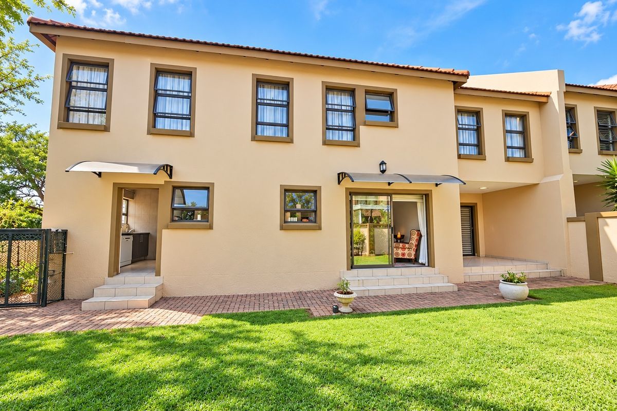 Rear view of the townhouse featuring a paved patio, well-maintained lawn, and multiple access points with modern awnings and secure window frames.