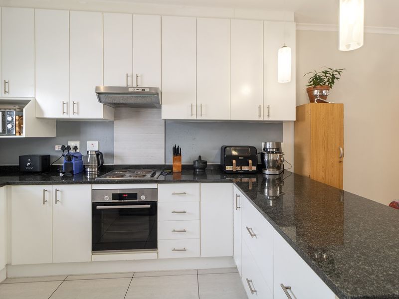 A functional kitchen featuring white cabinetry, dark granite countertops, built-in oven, hob, extractor fan, and tiled flooring.