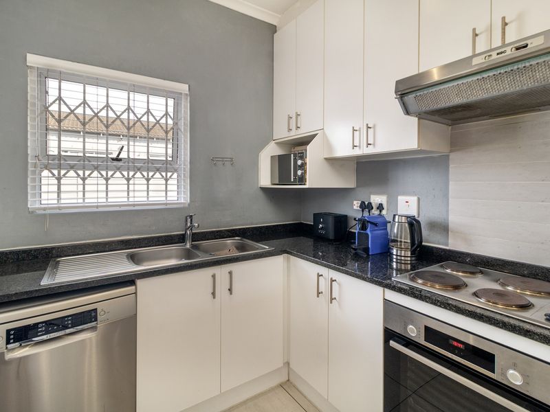 Compact kitchen featuring white cabinetry, granite countertops, integrated oven, electric hob, and extractor fan, with a security-fitted window.