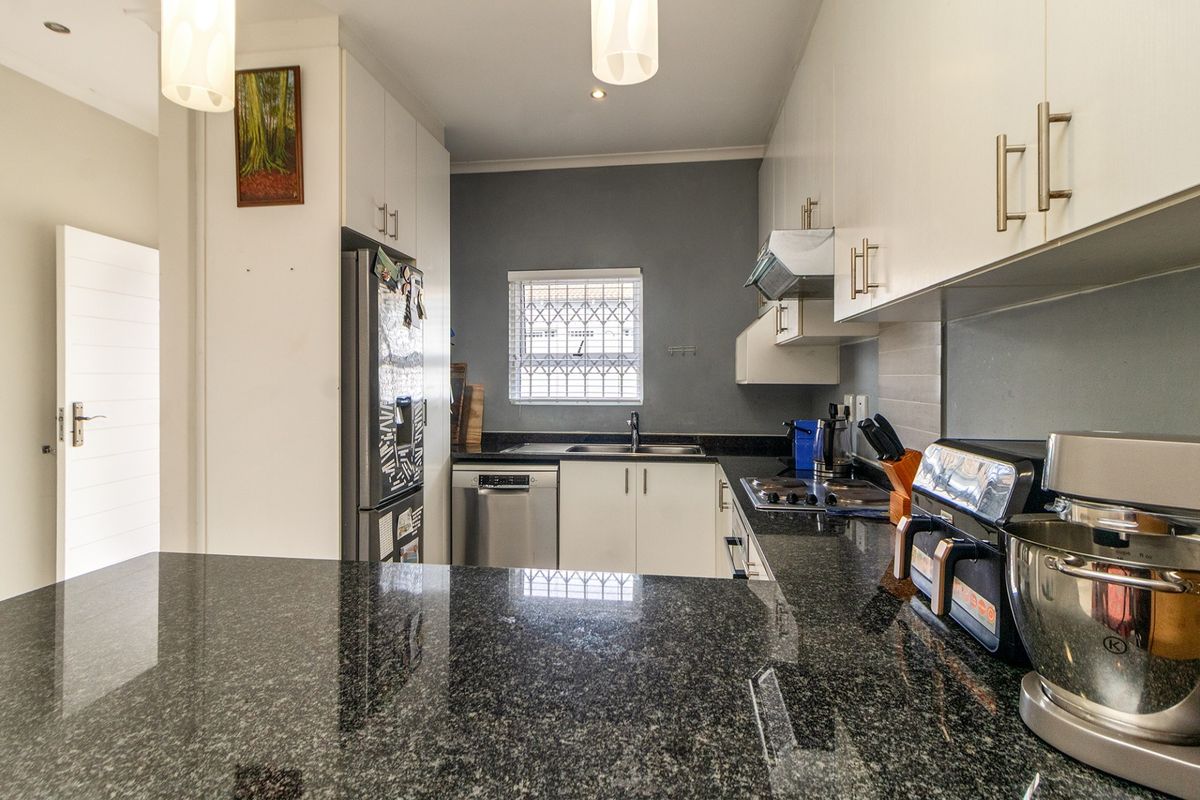 A functional kitchen featuring granite countertops, ample built-in cabinetry, a hob with extractor fan, and a window with security bars.