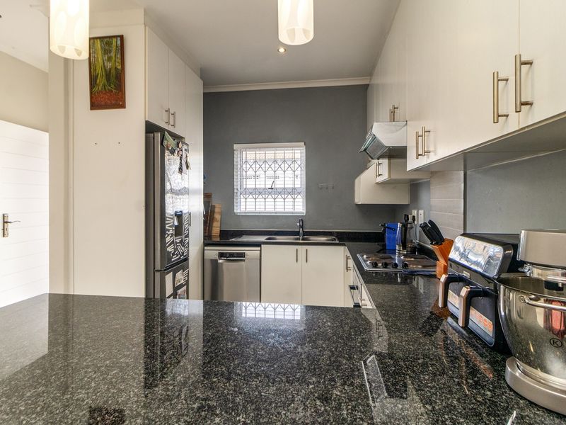 A functional kitchen featuring granite countertops, ample built-in cabinetry, a hob with extractor fan, and a window with security bars.