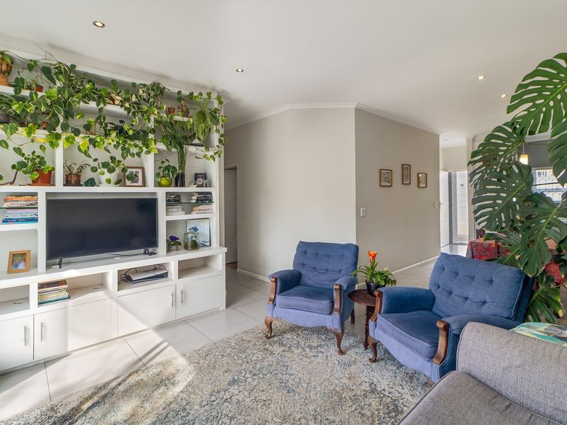 A bright living room featuring a large built-in white shelving unit, tiled flooring, and recessed downlighting.