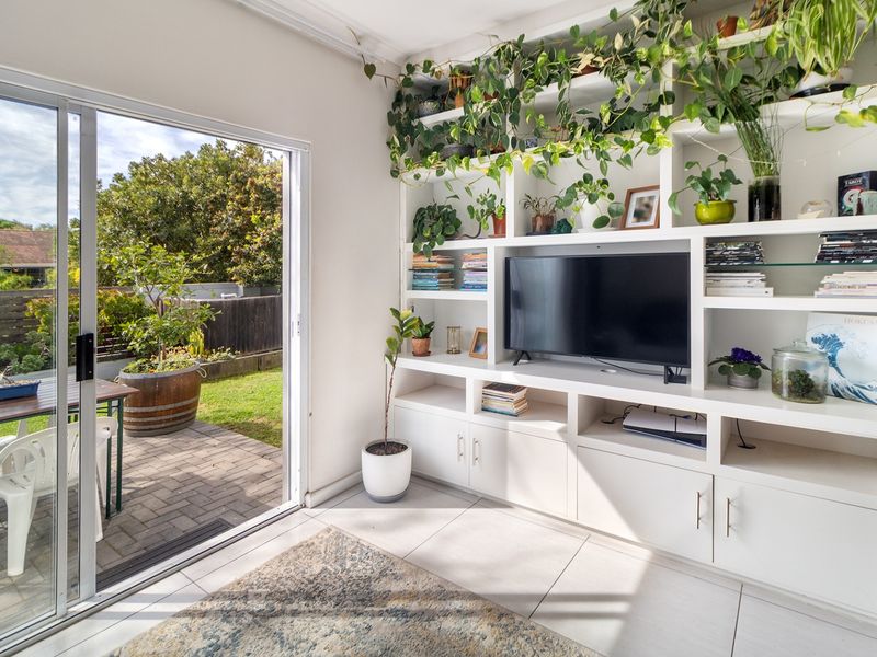 Bright living room featuring a large built-in shelving unit and a sliding glass door providing direct access to the paved patio and garden.