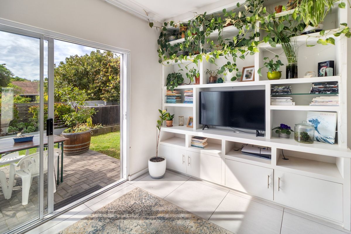 Bright living room featuring a large built-in shelving unit and a sliding glass door providing direct access to the paved patio and garden.