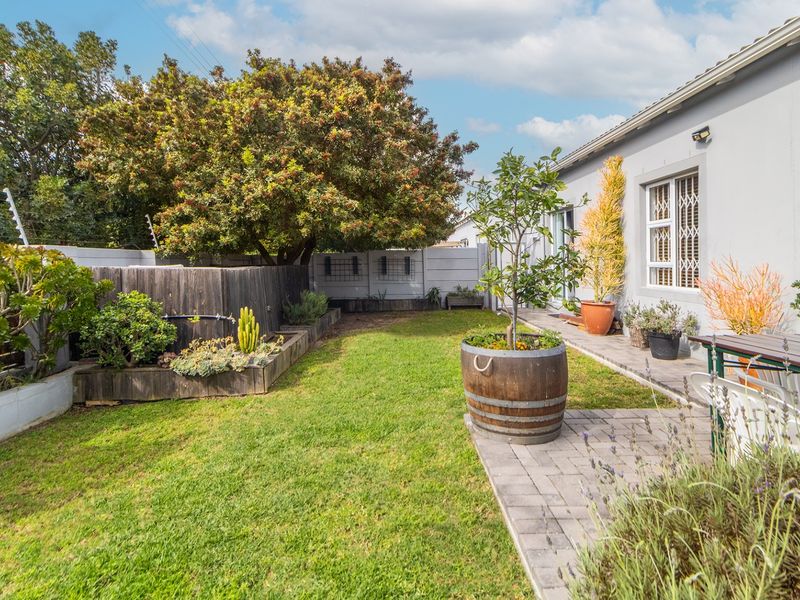 A well-maintained rear garden featuring a paved patio area, lush lawn, and secure boundary walls with electric fencing.