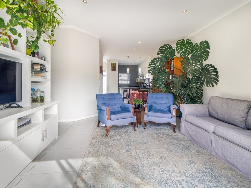 Open-plan living area featuring tiled flooring, recessed downlighting, and a custom built-in shelving unit, flowing seamlessly into the kitchen space.