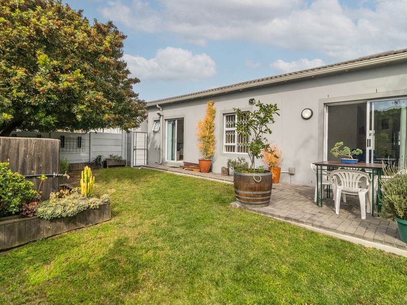A well-maintained rear garden featuring a paved patio area, established lawn, and direct access to the home via sliding glass doors.