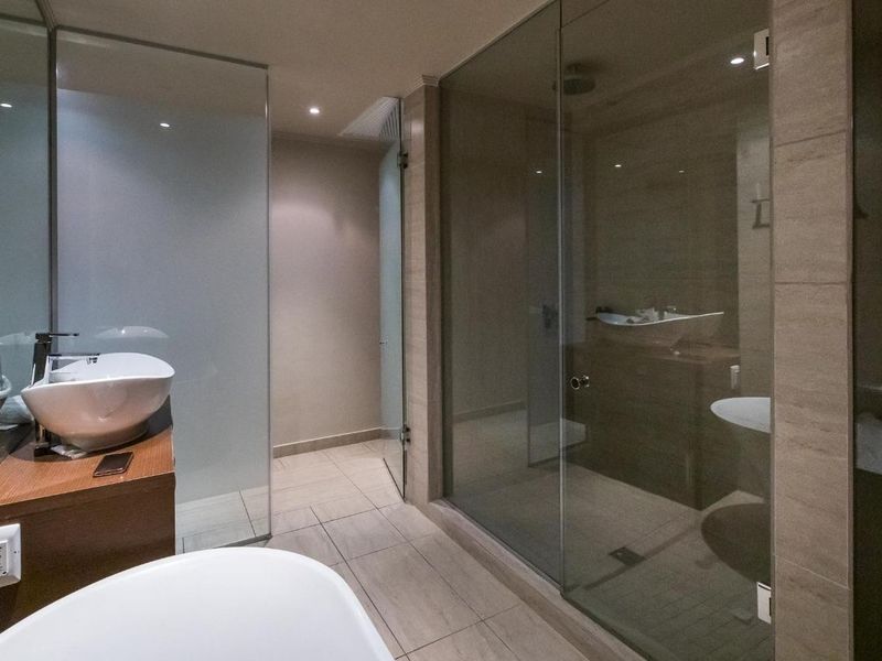 Modern bathroom featuring a glass-enclosed shower, vessel sink with wall-mounted faucet, and neutral tiled finishes.