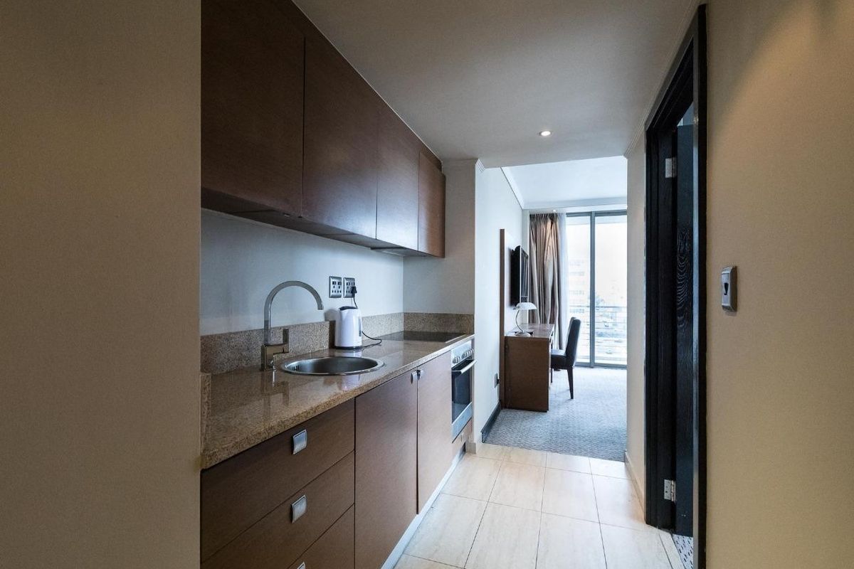 Compact kitchen featuring dark wood cabinetry, stone countertops, and integrated oven, leading into a bright living area with balcony access.