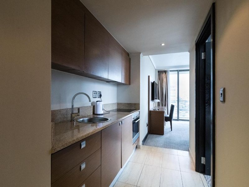 Compact kitchen featuring dark wood cabinetry, stone countertops, and integrated oven, leading into a bright living area with balcony access.