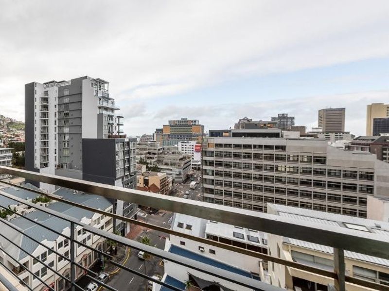 A spacious covered balcony featuring tiled flooring and a metal balustrade, offering expansive views of the surrounding city skyline.