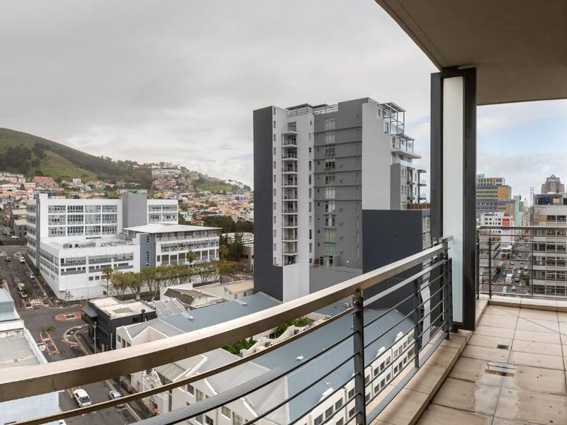 A spacious apartment balcony featuring tiled flooring and a metal railing, offering expansive urban views of the surrounding city and mountain landscape.