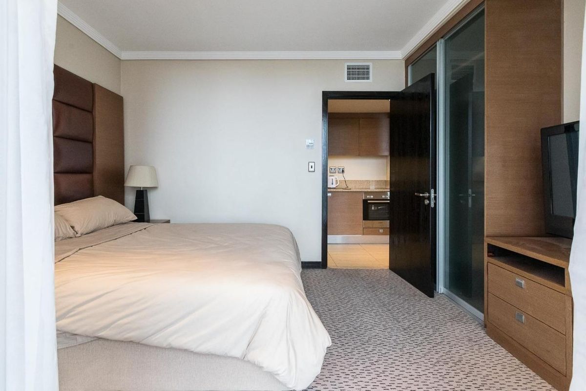 A well-maintained bedroom featuring carpeted flooring, coving, and a built-in wardrobe, with an adjacent view into a functional kitchen area.