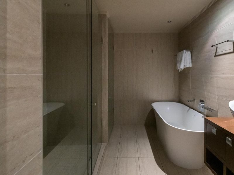Modern bathroom featuring a sleek freestanding bathtub, a spacious glass-enclosed shower, and contemporary wall-mounted basin with neutral floor-to-ceiling tiling.