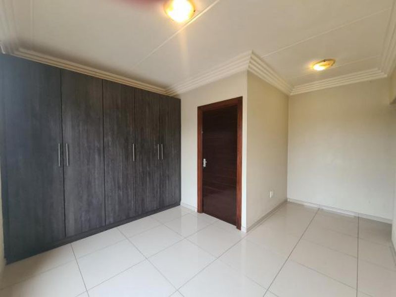 A bright, empty bedroom featuring modern dark wood built-in cupboards, neutral tiled flooring, and clean white walls with decorative ceiling cornices.