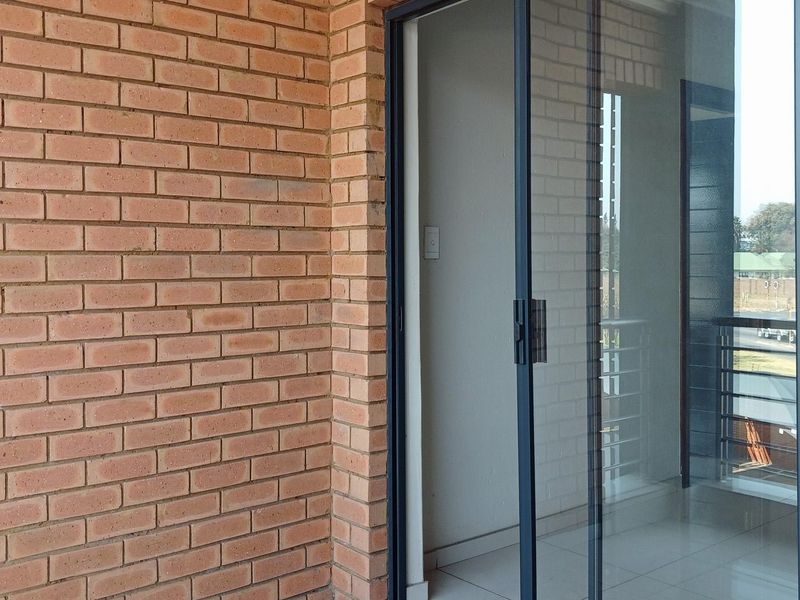 A clean, modern balcony featuring exposed brickwork, tiled flooring, and a sliding glass door, offering a bright and functional outdoor space.
