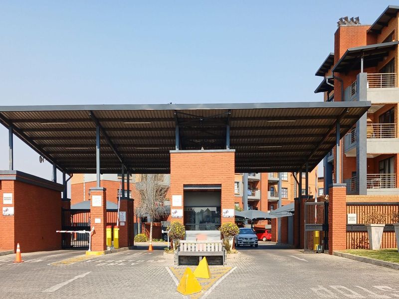 A secure gated entrance to the townhouse complex featuring a brick guardhouse, metal canopy, and controlled boom gate access.