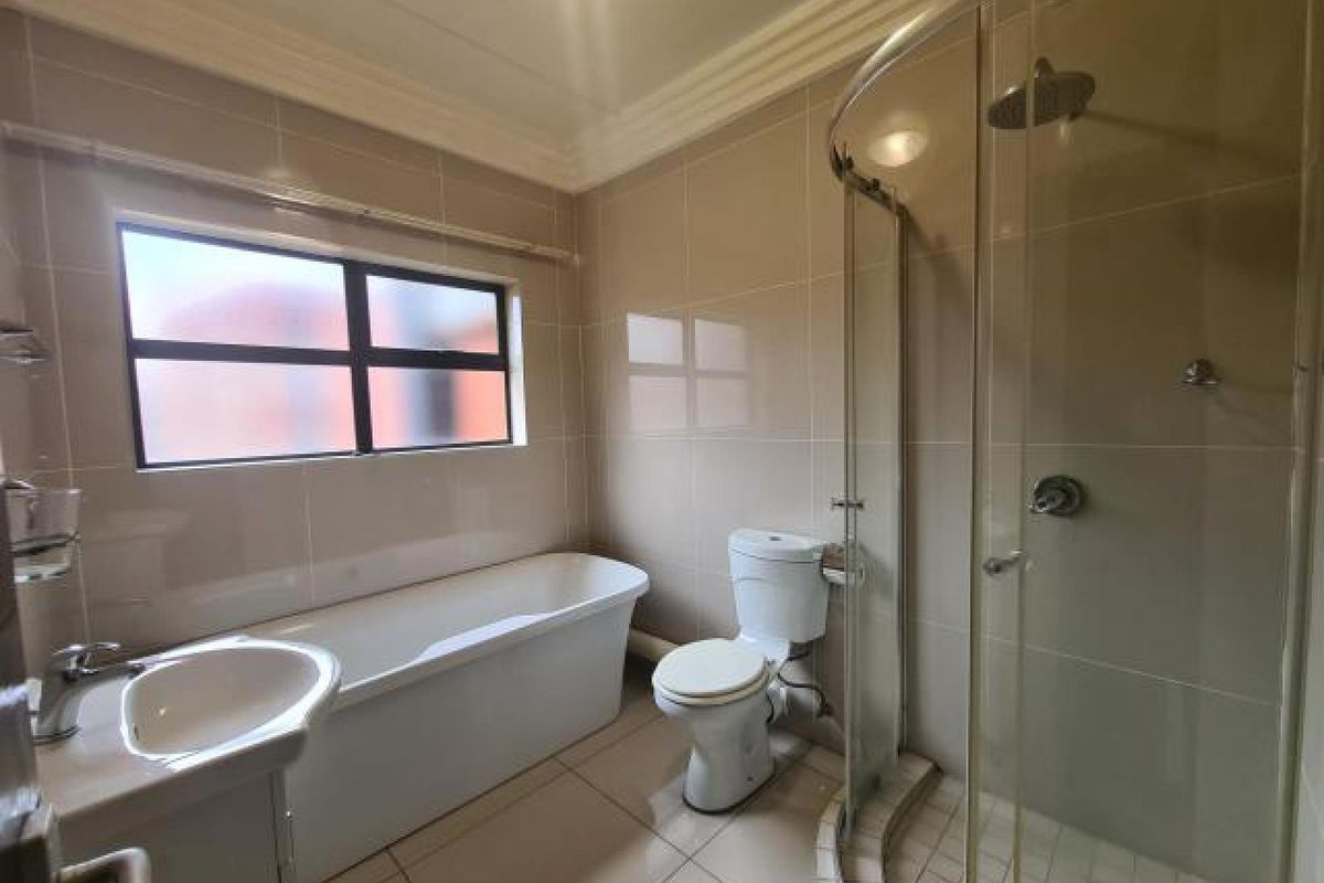 A clean, modern bathroom featuring a freestanding bathtub, a separate curved glass shower enclosure, a vanity basin, and neutral floor-to-ceiling wall tiles.