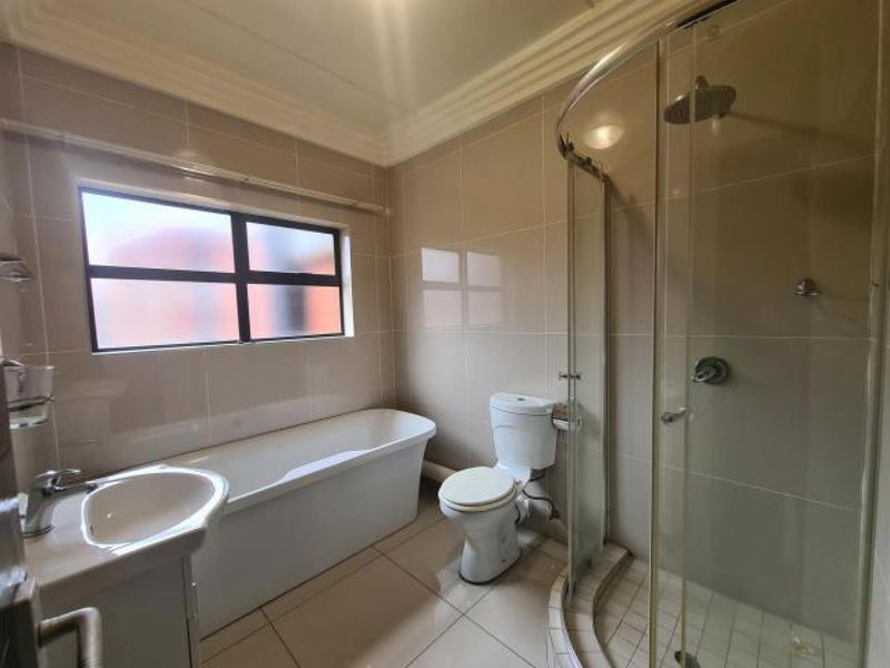 A clean, modern bathroom featuring a freestanding bathtub, a separate curved glass shower enclosure, a vanity basin, and neutral floor-to-ceiling wall tiles.