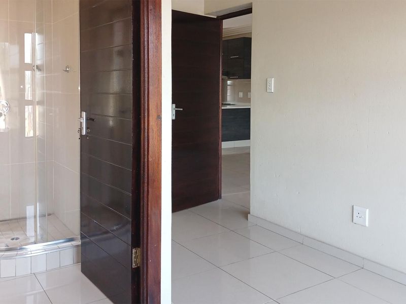 A clean, tiled hallway area providing access to a shower room and an adjacent living space with dark wood doors.