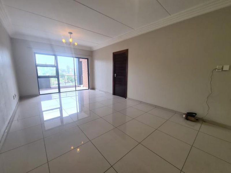 A bright, empty living room featuring large format floor tiles, a sliding glass door leading to a balcony, and neutral wall finishes.