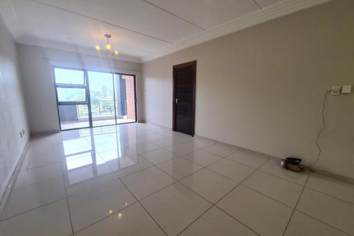 A bright, empty living room featuring large format floor tiles, a sliding glass door leading to a balcony, and neutral wall finishes.