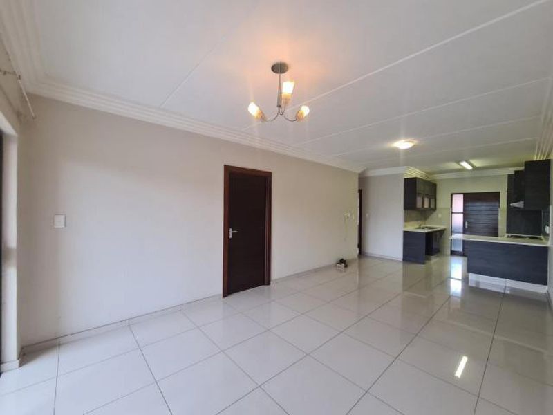 Spacious open-plan living area featuring large format floor tiles, neutral walls, and a modern kitchen with built-in cabinetry and a breakfast bar.