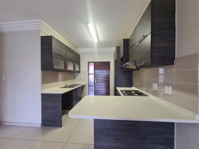Modern kitchen featuring dark wood cabinetry, white stone countertops, integrated electric hob, extractor fan, and tiled backsplash in a clean, open layout.