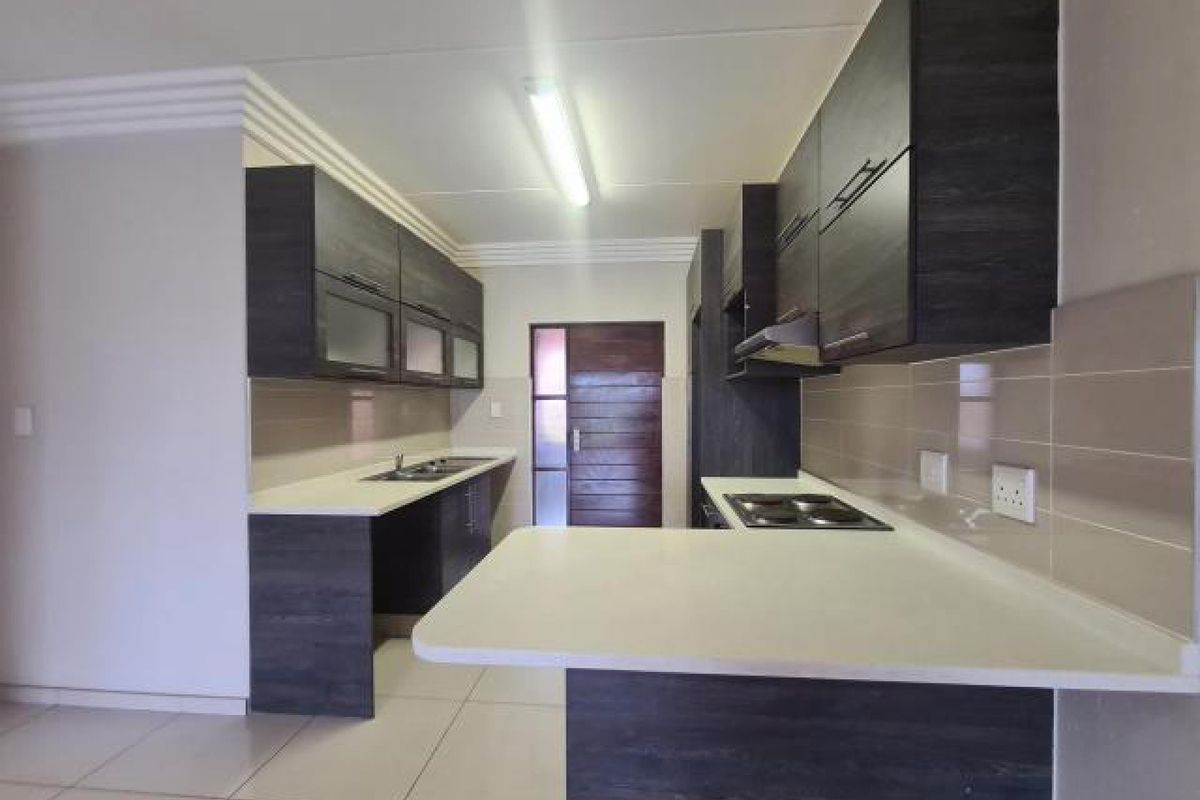 Modern kitchen featuring dark wood cabinetry, white stone countertops, integrated electric hob, extractor fan, and tiled backsplash in a clean, open layout.