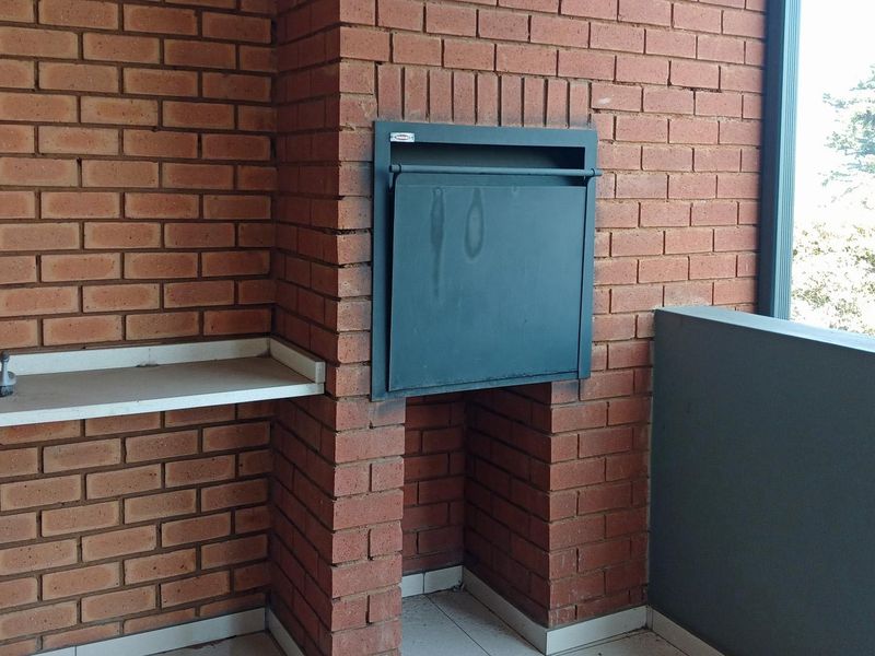 Covered balcony area featuring a built-in brick braai, tiled flooring, and a metal balustrade, offering a functional outdoor entertainment space.
