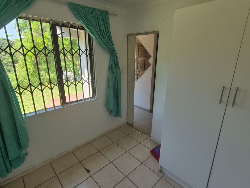 A vacant bedroom featuring tiled flooring, a built-in wardrobe, and a window fitted with a security gate.