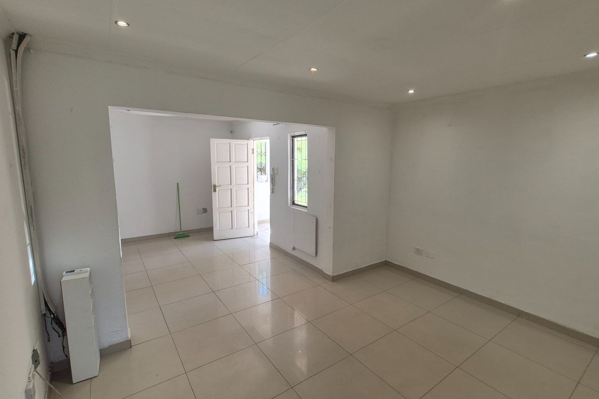 An empty, open-plan living area featuring neutral tiled flooring, recessed lighting, and a wall-mounted panel heater, providing a blank canvas for interior design.