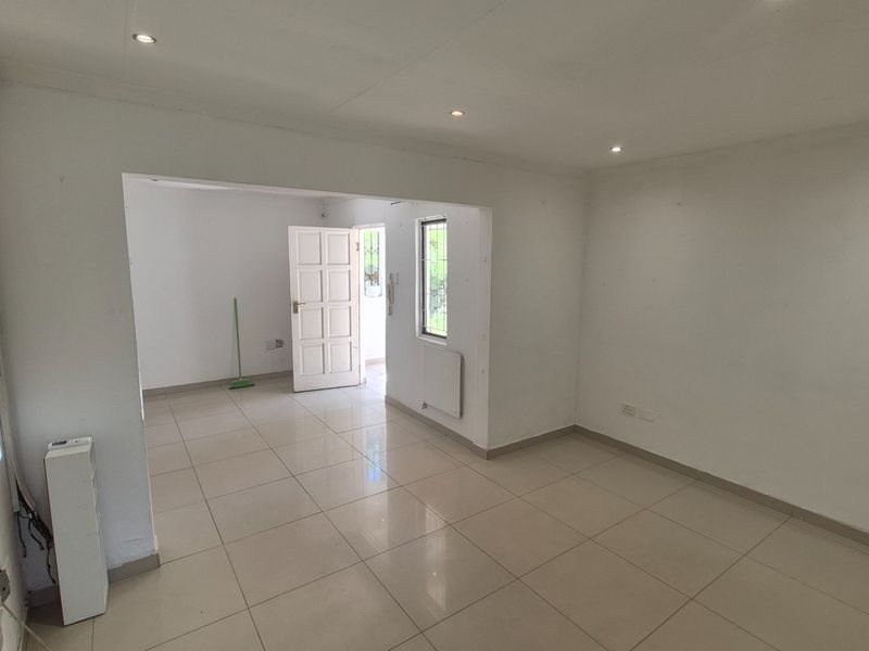 An empty, open-plan living area featuring neutral tiled flooring, recessed lighting, and a wall-mounted panel heater, providing a blank canvas for interior design.