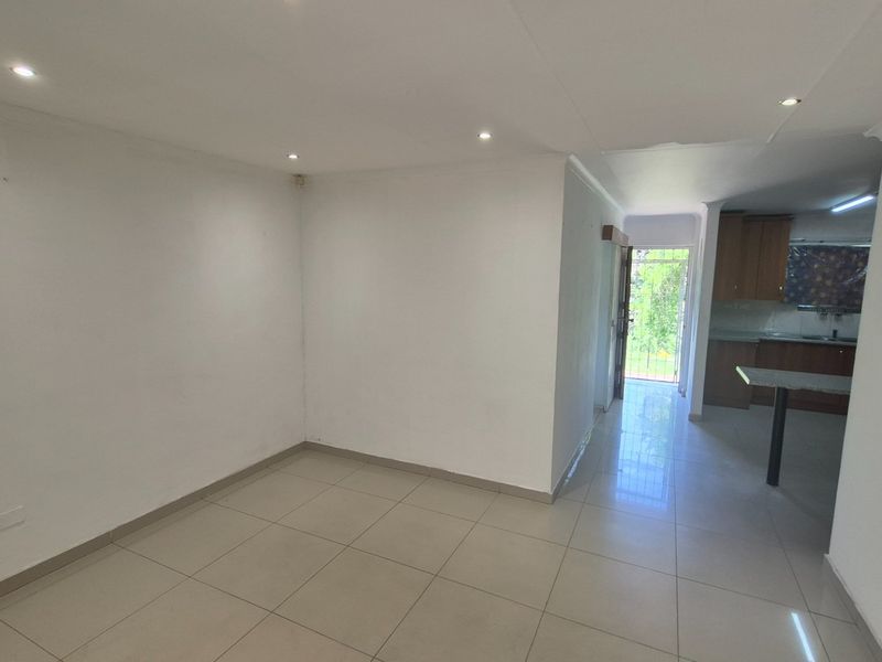 An open-plan living area featuring tiled flooring and recessed lighting, flowing into a kitchen space with built-in cabinetry and direct access to the exterior.