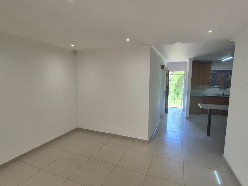 An open-plan living and kitchen area featuring tiled flooring, recessed lighting, and neutral walls, leading to an exterior security gate.