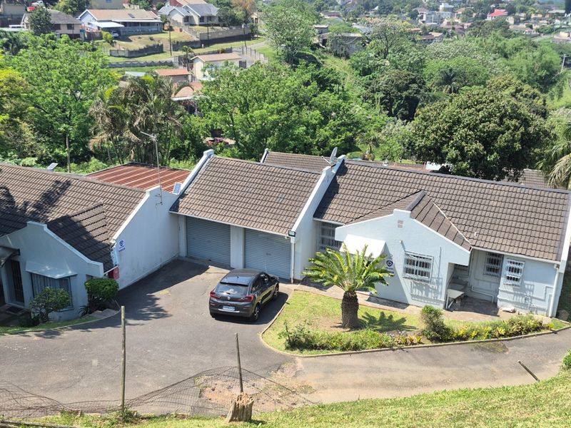 Aerial view of a residential property featuring a tiled roof, double garage, and paved driveway, set within a suburban landscape.