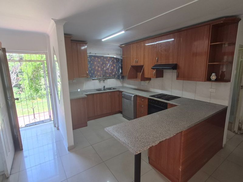 Functional kitchen featuring wood-finish cabinetry, granite countertops, integrated hob and oven, and direct access to the exterior via a security gate.