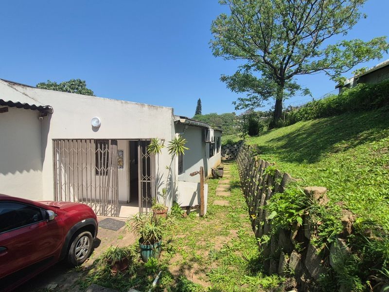 Rear exterior view of the property featuring a paved pathway, security gate, and a stone retaining wall bordering the sloped garden area.