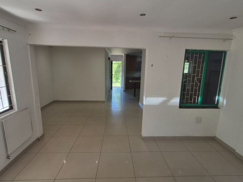 An open-plan living area featuring neutral tiled flooring, recessed lighting, and security bars on the windows, offering a blank canvas for interior design.