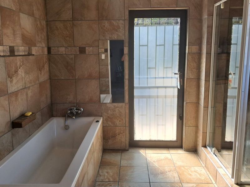 A spacious bathroom featuring full-height wall tiling, a built-in bathtub, a separate shower enclosure, and a frosted glass door leading to the exterior.