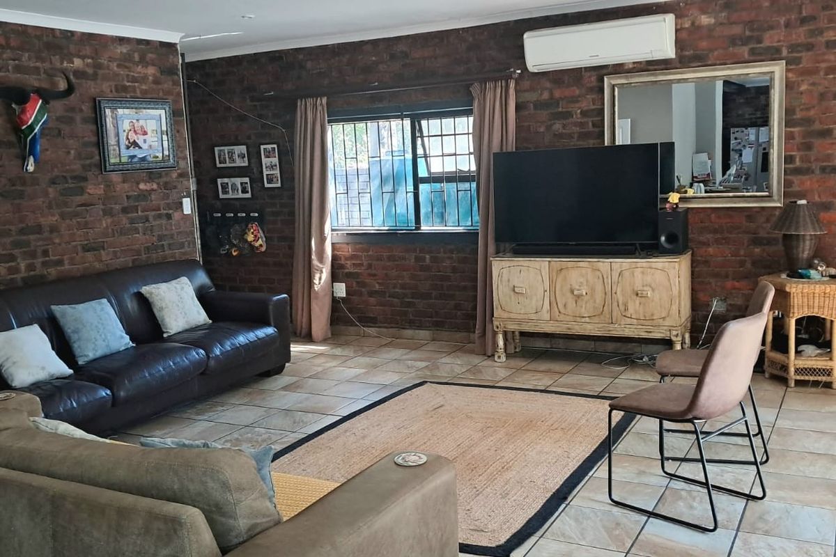 A living room featuring exposed brick walls, tiled flooring, and a wall-mounted air conditioning unit, providing a rustic and functional living space.