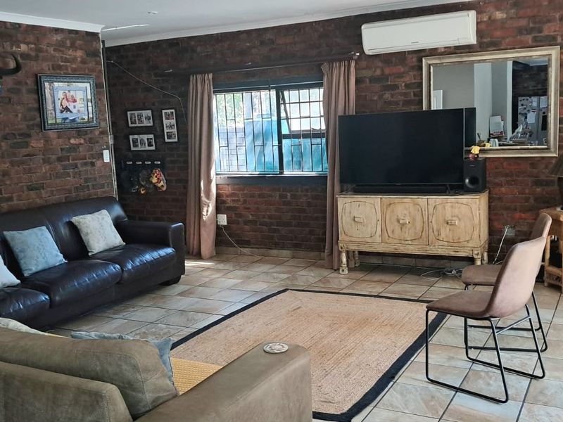 A living room featuring exposed brick walls, tiled flooring, and a wall-mounted air conditioning unit, providing a rustic and functional living space.