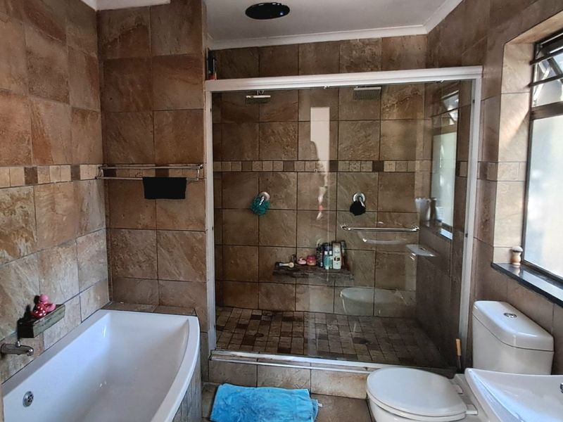 A functional bathroom featuring a built-in bathtub, a separate walk-in shower with a glass enclosure, a toilet, and a washbasin with tiled finishes.