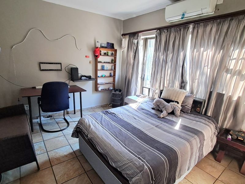 A functional bedroom featuring tiled flooring, a wall-mounted split-system air conditioner, and large windows with curtain rails.